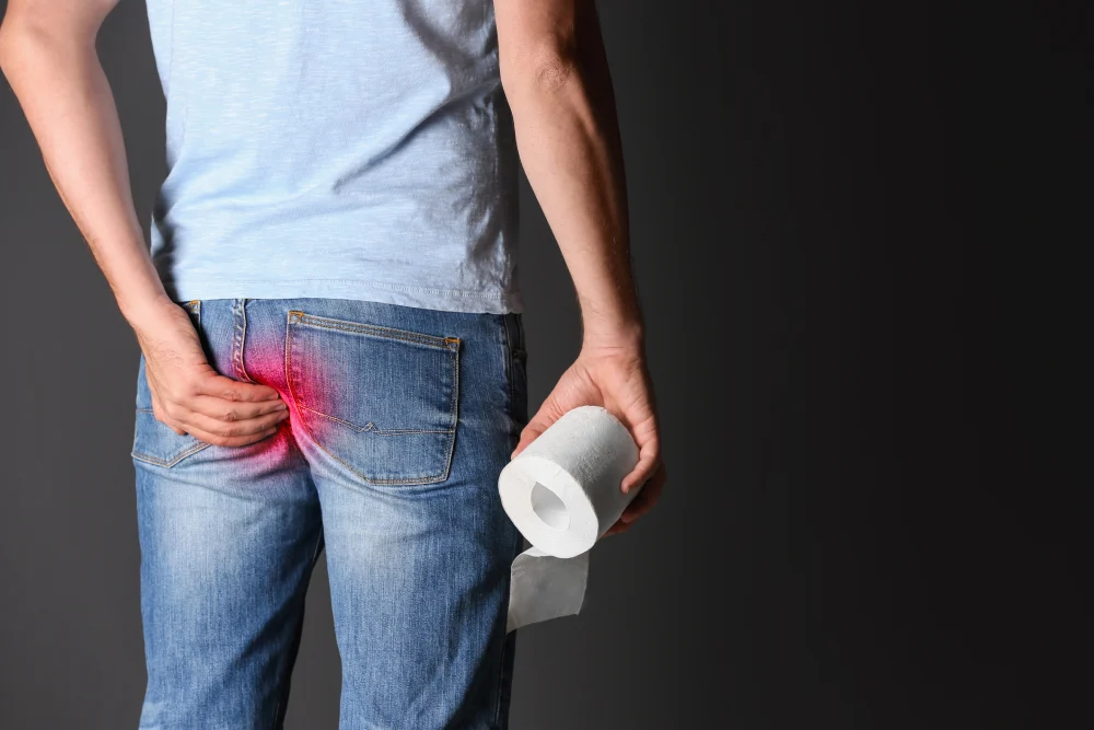 Man holding a toilet roll while experiencing discomfort associated with piles.